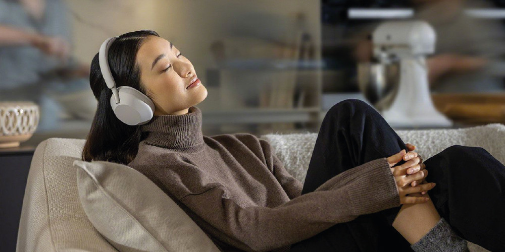 Persoon ontspant op de bank met koptelefoon op, genesteld in comfortabele kleding.
