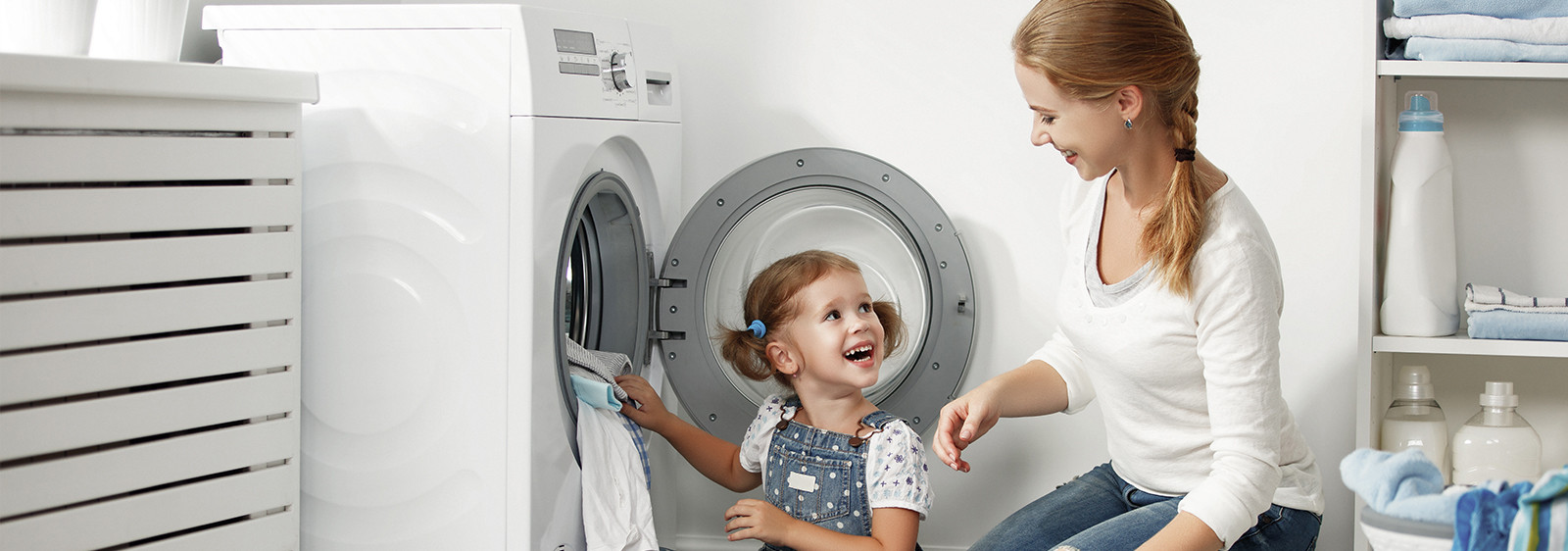 Een vrouw en een kind zijn samen bezig met het in- of uitladen van een wasmachine in een wasruimte.
