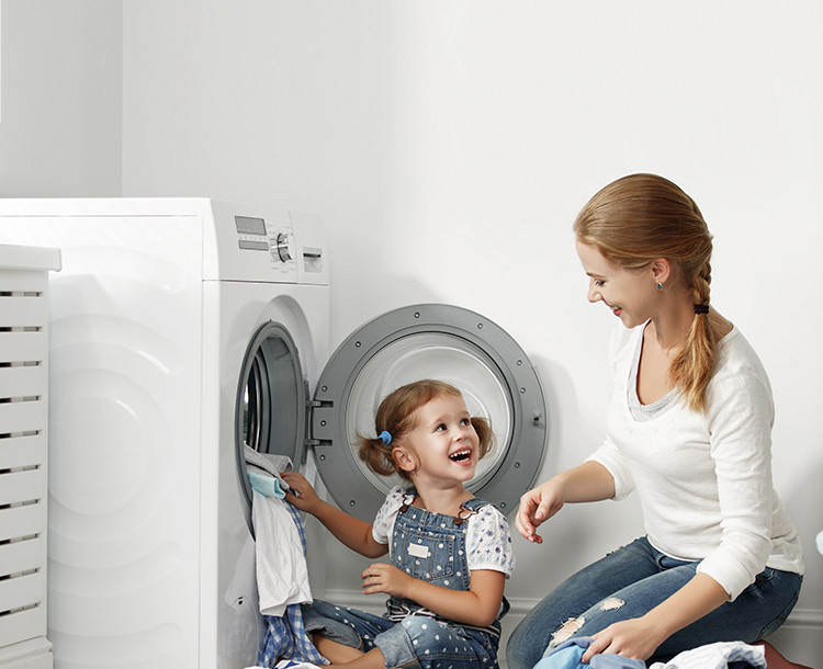 Moeder en kind doen samen de was naast een open wasmachine.