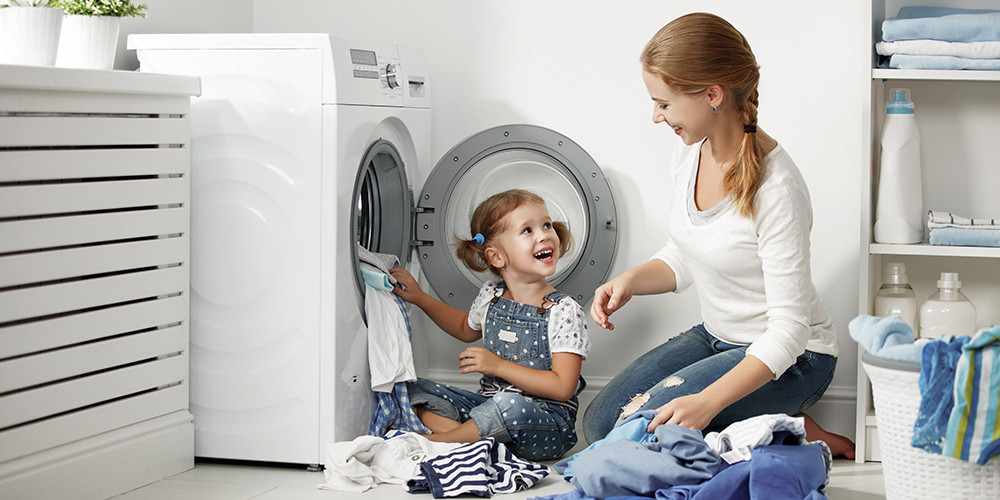 Een vrouw en kind doen samen de was naast een open wasmachine.