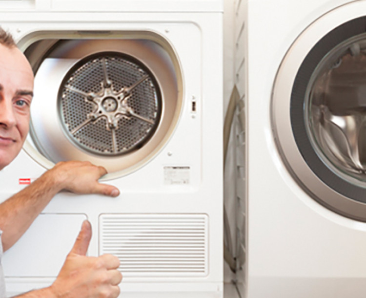 Man wijst glimlachend naar een open wasmachine of droger en steekt zijn duim omhoog.