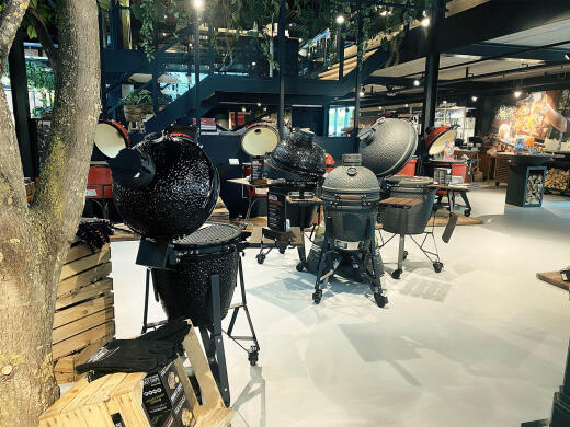 Verschillende kamado barbecues in een showroom met moderne inrichting en bomen.
