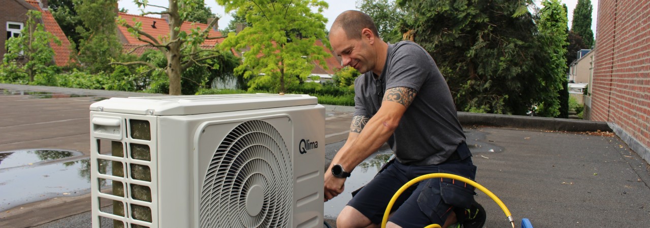 Persoon onderhoudt een airconditioning unit op een dak.