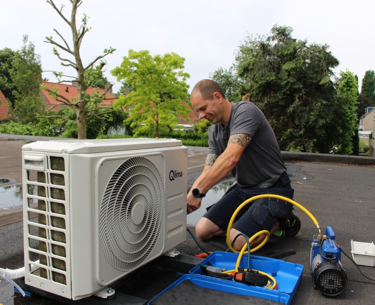 Persoon onderhoudt een airconditioning unit op een dak.