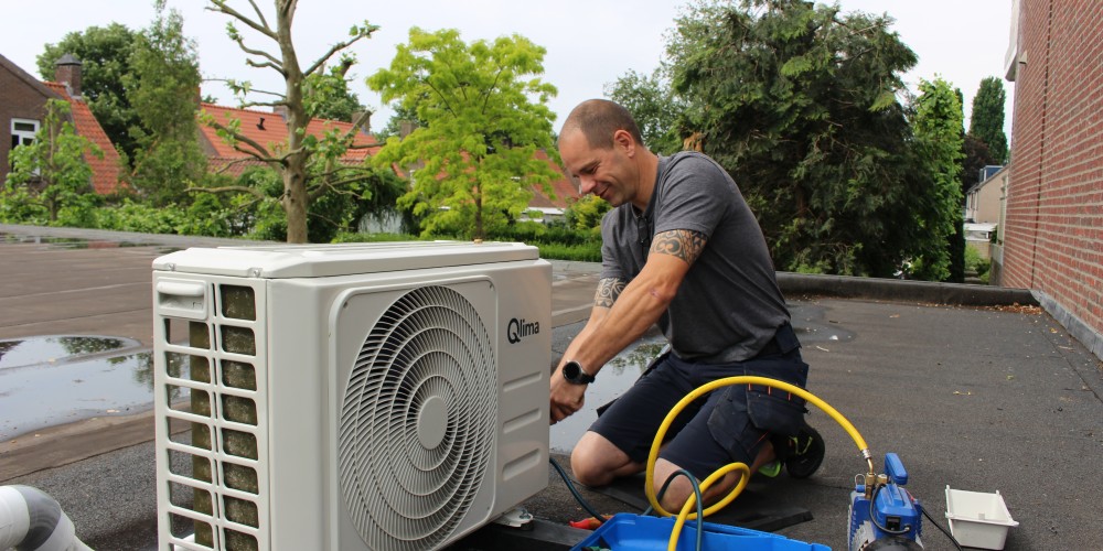 Man werkt aan airconditioningunit op plat dak met gereedschap in de buurt.