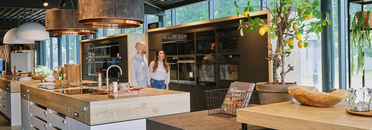 Moderne keuken met twee mensen, kookeilanden, planten en ingebouwde ovens.