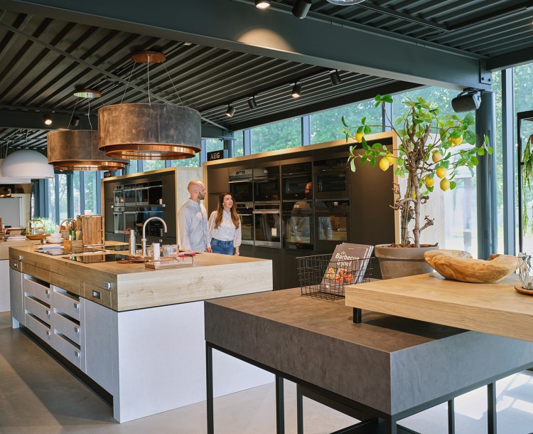 Moderne keuken met twee mensen, kookeilanden, planten en ingebouwde ovens.