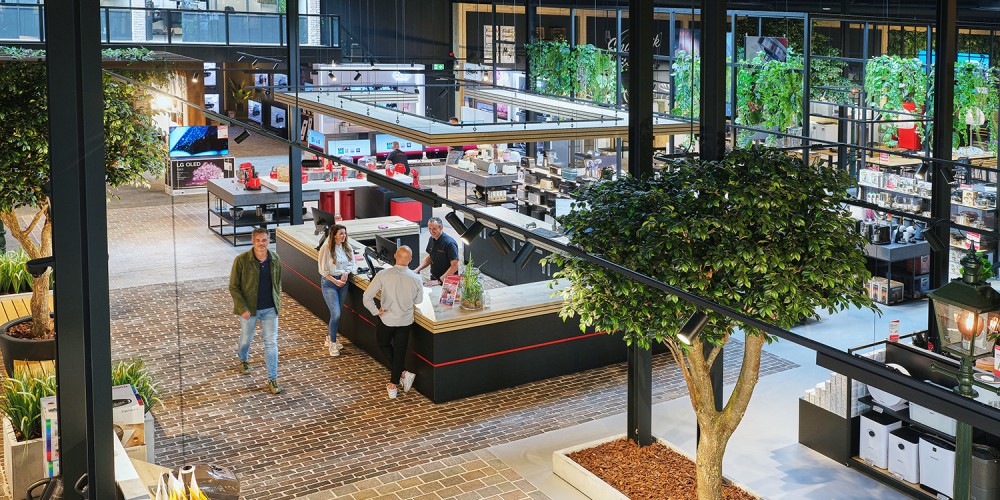 Winkelinterieur met mensen, groen decor, en elektronica-displays op een open, moderne locatie.