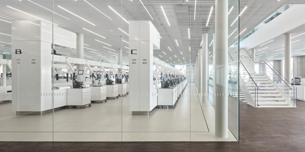 Grote, moderne, glazen laboratoriumruimte met witte werkstations en een trap op de achtergrond.