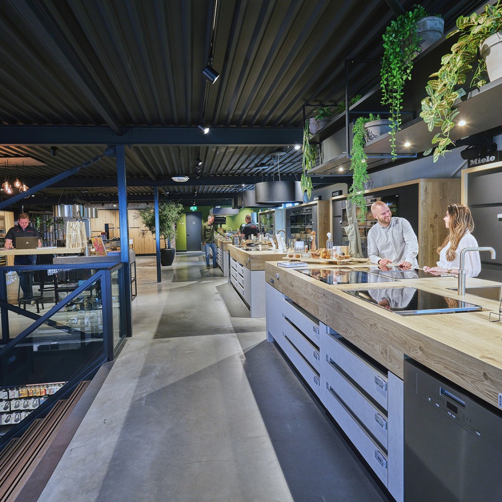 Moderne keukenwinkel met mensen aan het werk; keukenapparatuur en planten aanwezig.