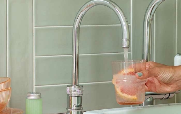 Een hand houdt een glas vol fruit onder stromend water bij een kraan.