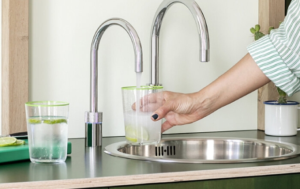 Een hand houdt een glas onder een kraan bij een wasbak, met een ander glas naast de kraan.