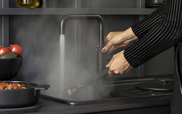 Persoon spoelt een bakplaat af onder een kraan met stromend water in een moderne keuken.
