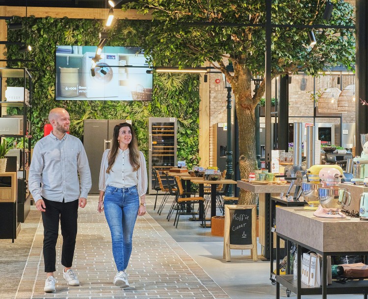 Een paar mensen in een moderne winkel met elektronica en keukenspullen, omgeven door groen.