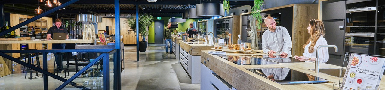 Keukenshowroom met mensen die keukens en apparaten bekijken en bespreken.