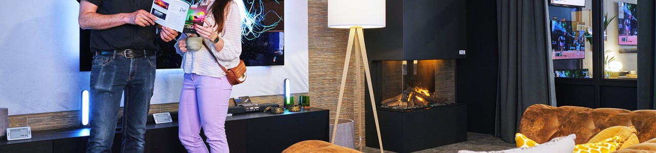 Een moderne woonkamer met haard, bank, vloerlamp en mensen die een brochure lezen.