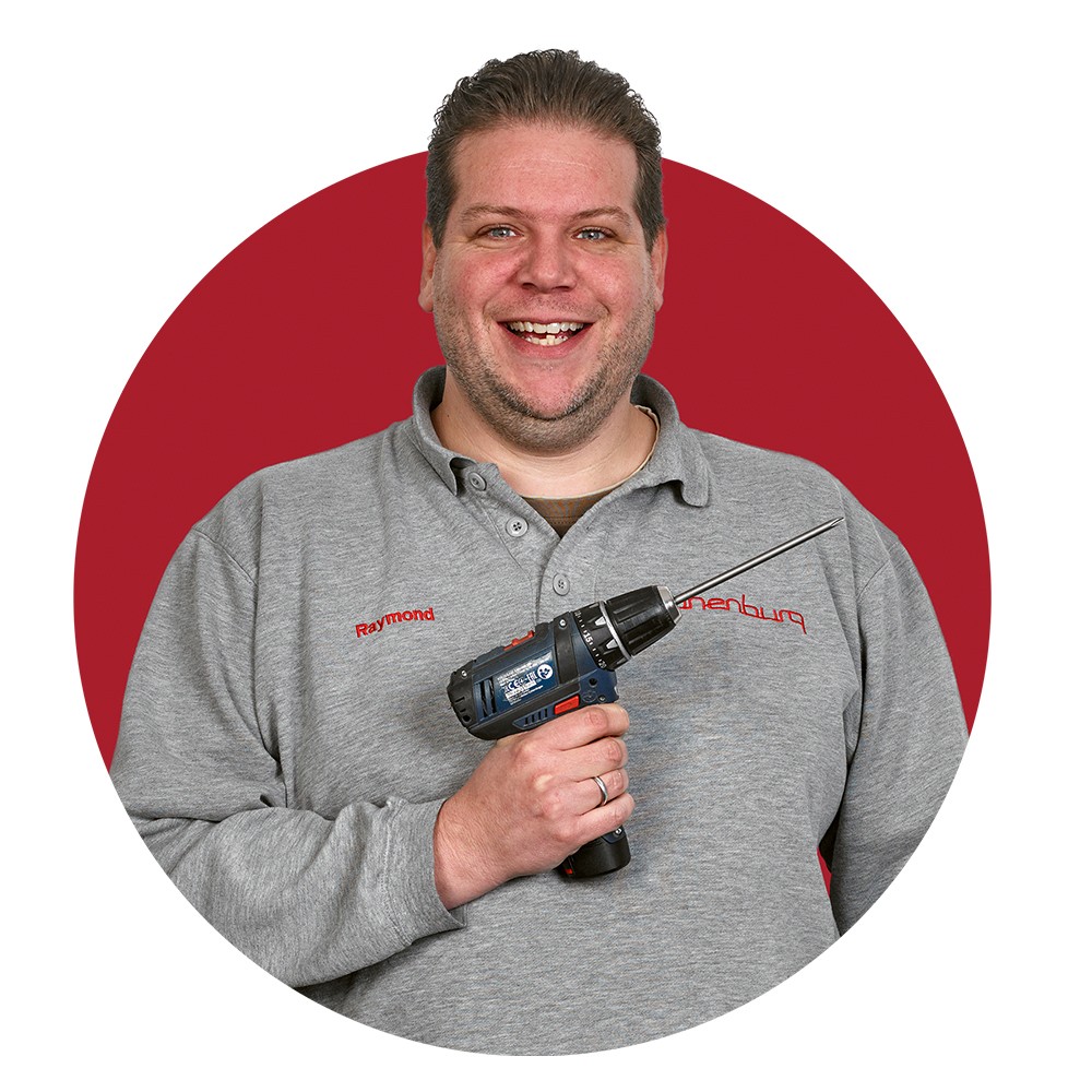 Persoon in een grijze trui die een boormachine vasthoudt voor een rode achtergrond.