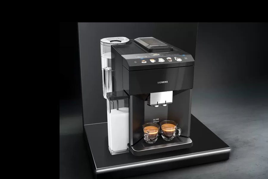 Koffiezetapparaat met twee gevulde koffiekopjes en een melkreservoir op een donker achtergrond.