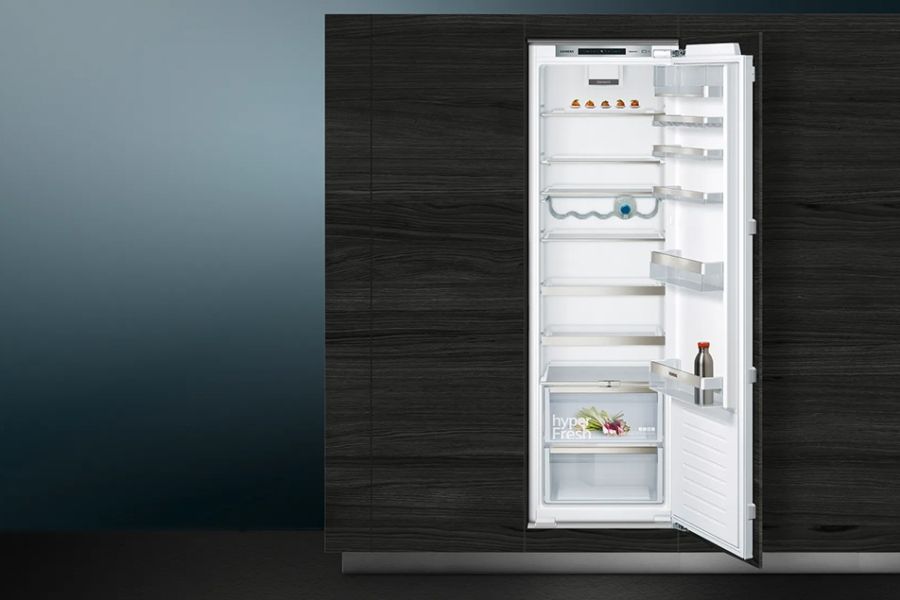 Ingebouwde koelkast met open deur, gedeeltelijk gevuld, tegen een donkere houten achtergrond.