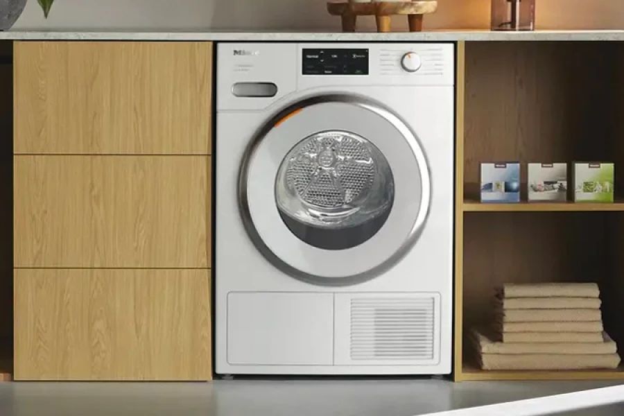 Wasmachine in keuken ingebouwd tussen houten kasten met daarnaast opgestapelde handdoeken en boeken.