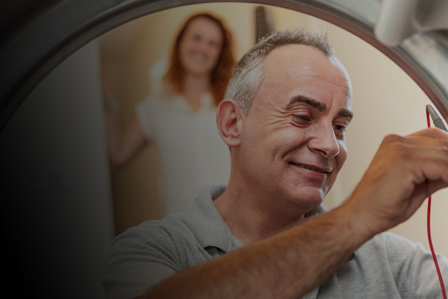 Man repareert een apparaat terwijl een vrouw op de achtergrond kijkt.