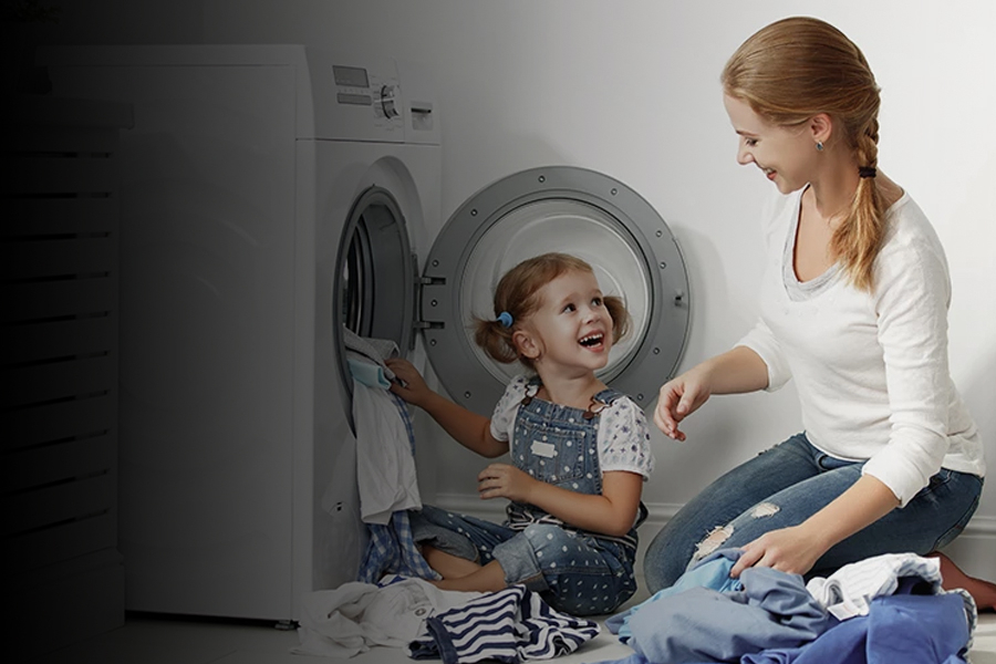 Moeder en kind doen samen de was, zittend bij een wasmachine.