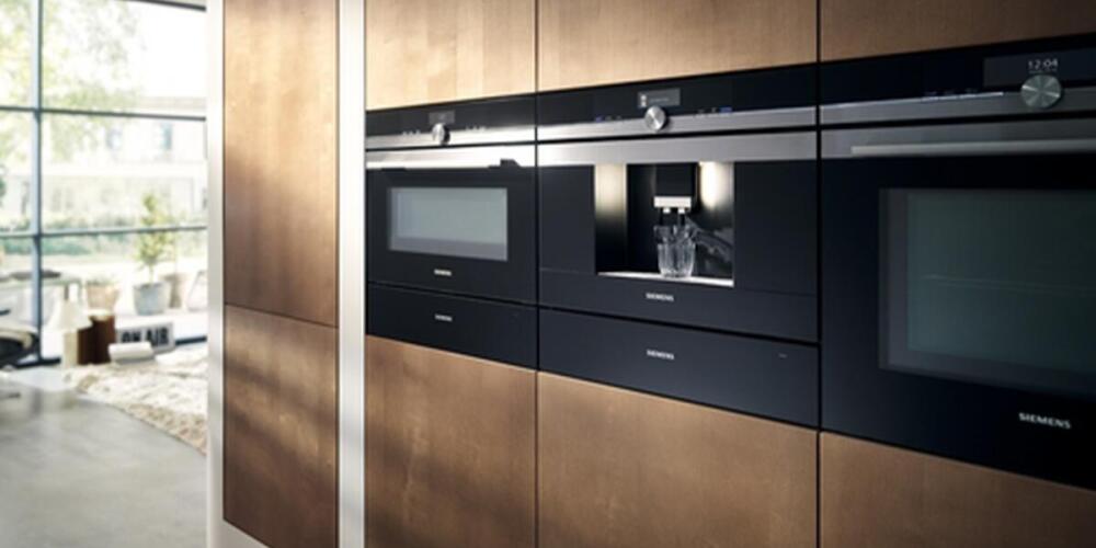 Moderne keukenapparatuur ingebouwd in houten kastenwand, inclusief ovens en koffiezetapparaat.